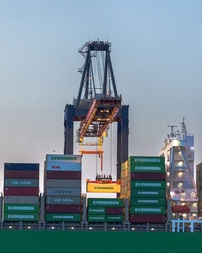 A busy container crane in Rotterdam port handling international cargo operations at dusk.