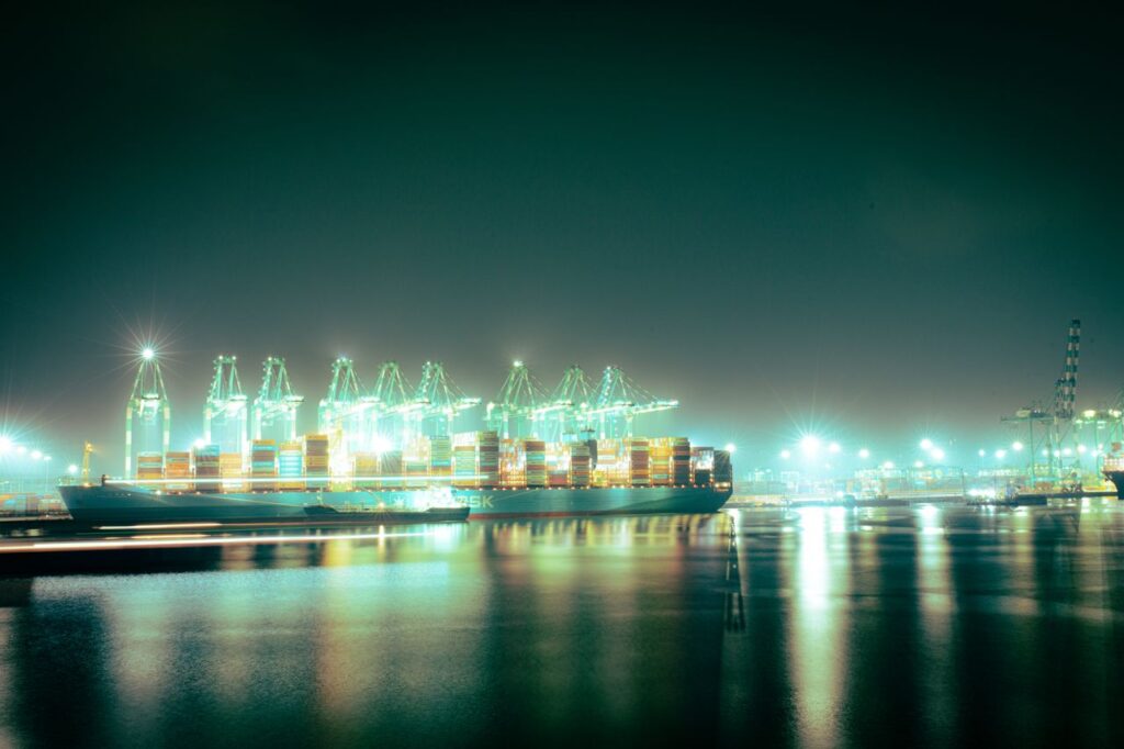 Stunning nighttime shot of a cargo ship in a brightly lit port with glowing cranes and reflections.